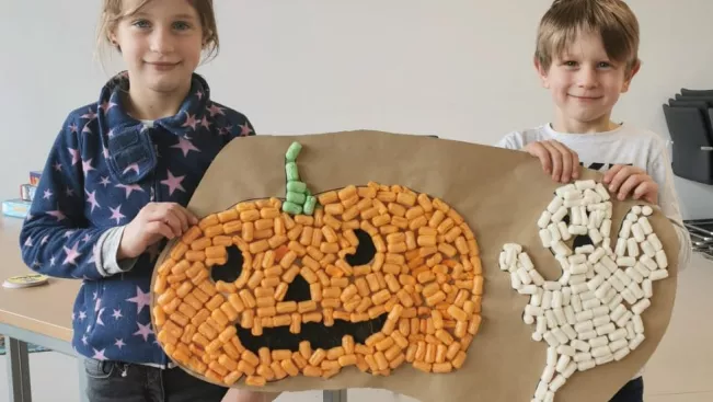 A girl and a boy with self-made picture from Playmais with the motives pumpkin and ghost.